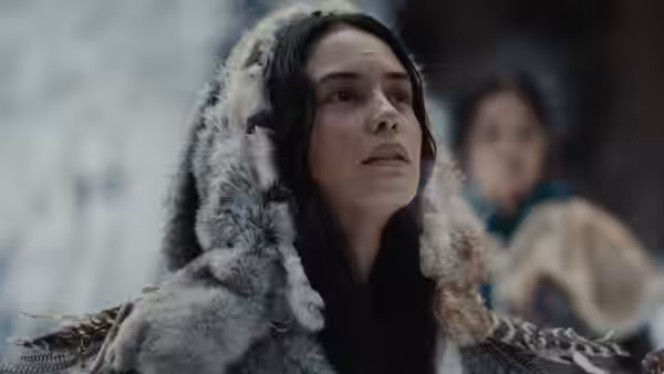 A woman wearing a fur-trimmed hood gazes upward in a snowy area