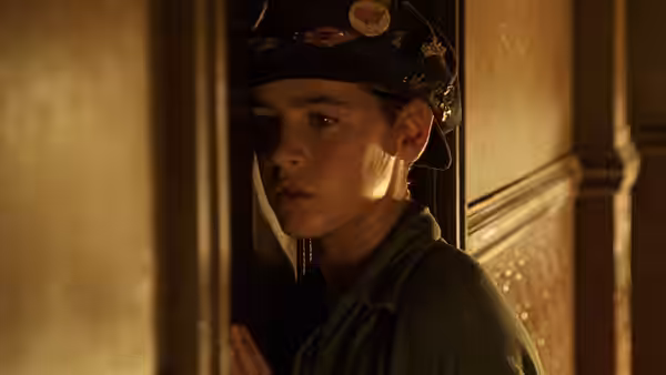 Boy in a cap with buttons peers from behind a wooden doorway