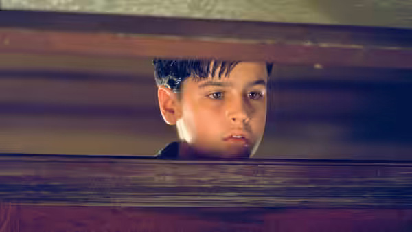 Young boy looks out from under a dark wooden piece of furniture