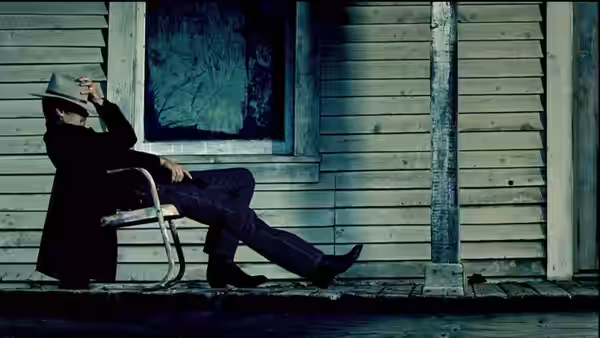 Raylan Givens (Timothy Olyphant) seated on a porch adjusting his hat