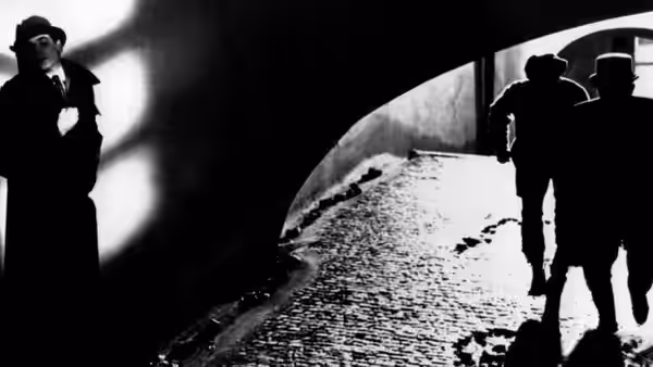 Kafka (Jeremy Irons) standing in shadow as two figures run down a tunnel