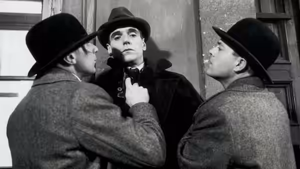 Kafka (Jeremy Irons) adjusting his collar between two men in bowler hats