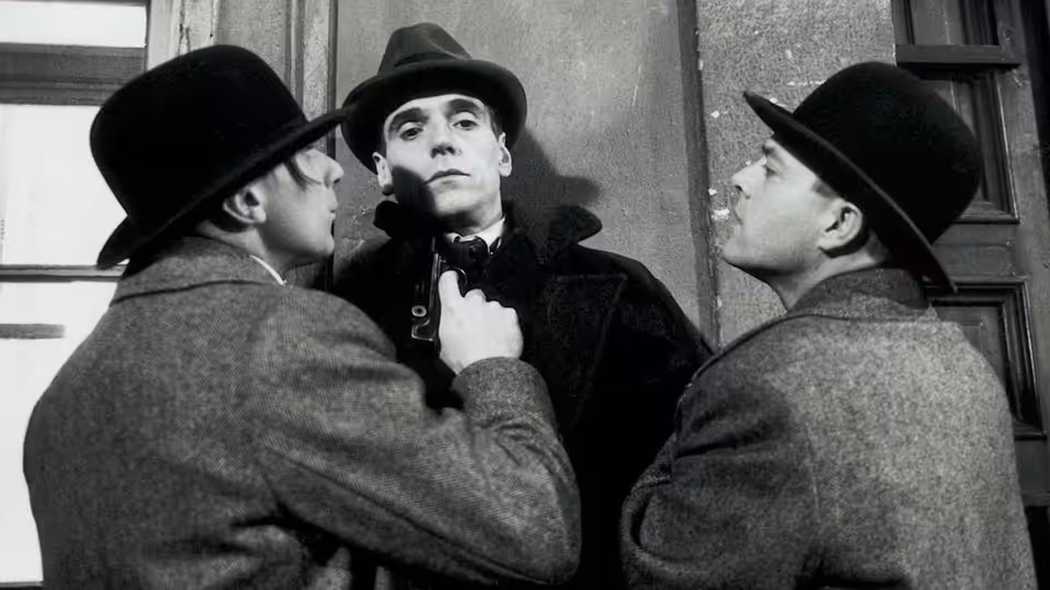 Kafka (Jeremy Irons) adjusting his collar between two men in bowler hats