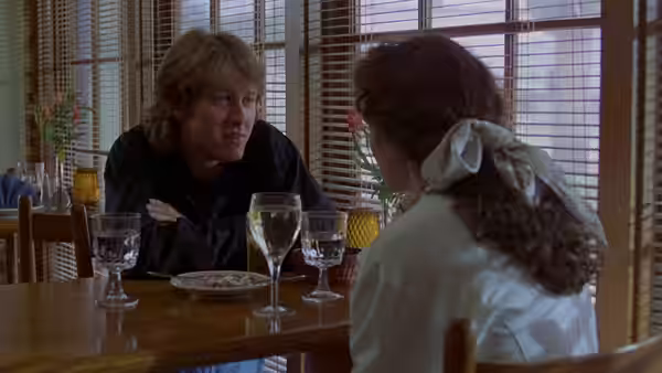 a blond man talks with a woman at a restaurant table
