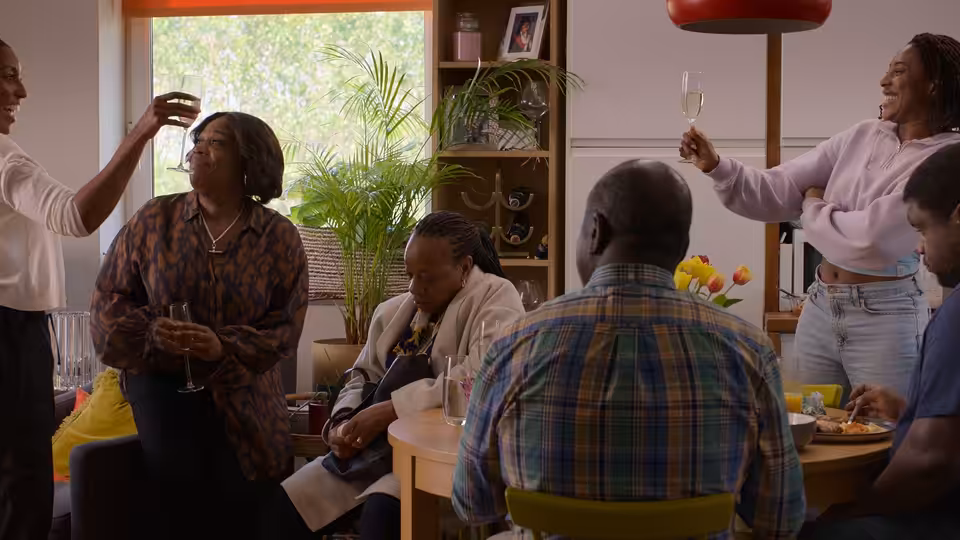 A group of friends and family gathered around a table raising glasses in a bright room