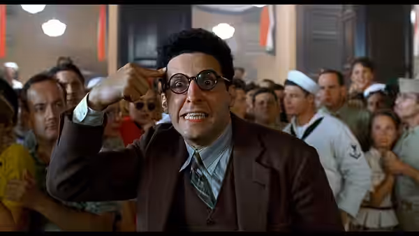 Barton Fink (John Turturro) gesturing with hand to head in crowded hall