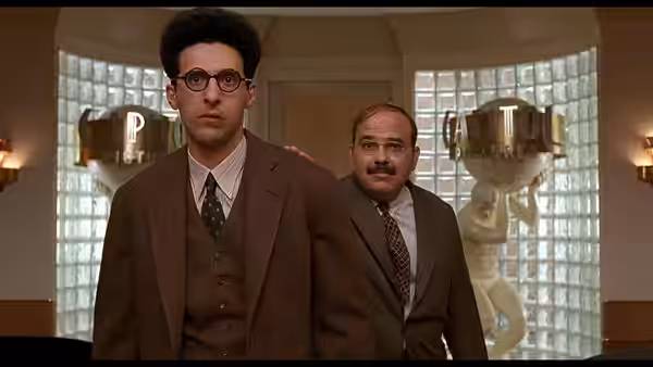 Barton Fink (John Turturro) stands with suited man in ornate lobby