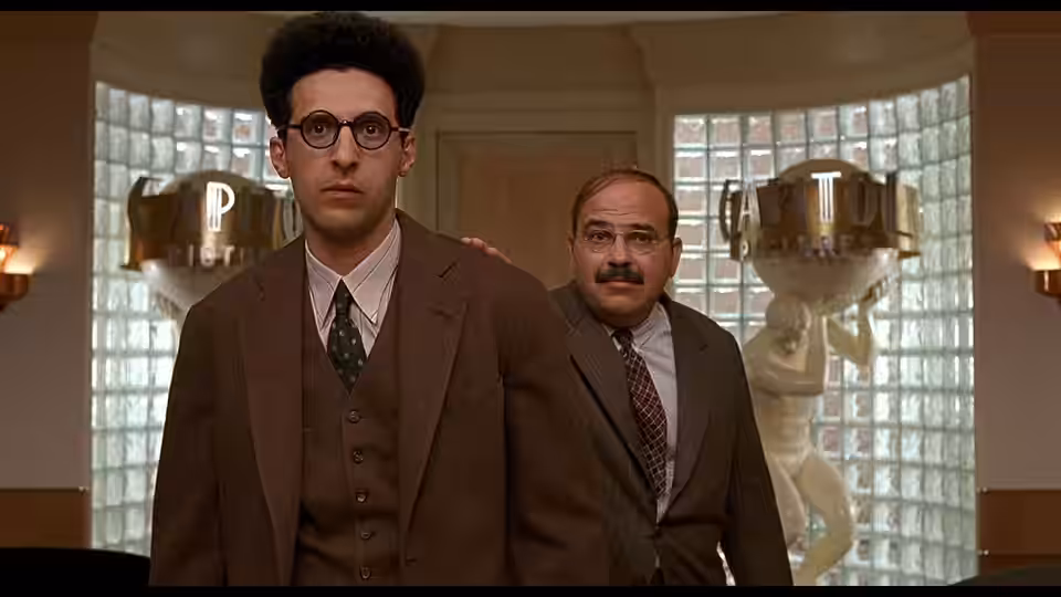 Barton Fink (John Turturro) stands with suited man in ornate lobby