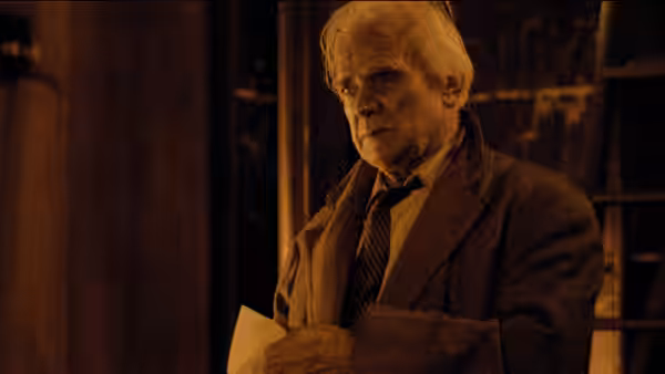 an older man in a coat holding papers and looking aside