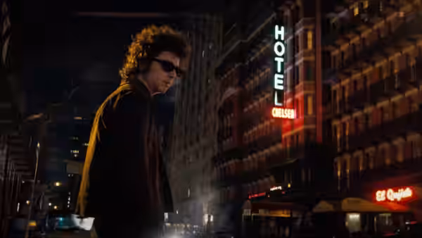 Bob Dylan (Timothée Chalamet) walks past the illuminated Chelsea Hotel sign