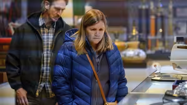 Woman in blue jacket standing at counter with man in background store