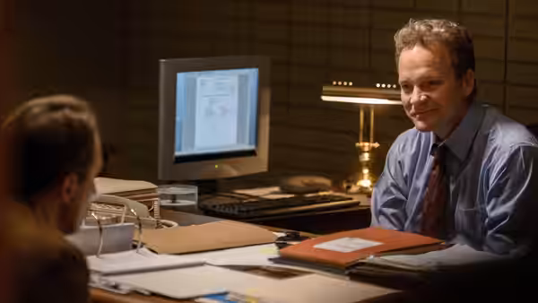 Man in blue shirt smiling at desk with old computer monitor