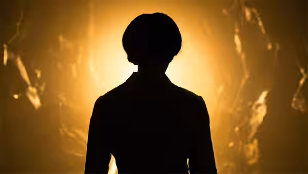 Silhouetted figure facing a glowing cracked wall from behind
