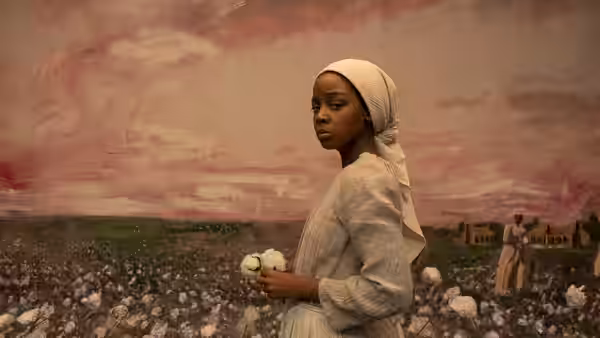 Cora (Thuso Mbedu) holding cotton bolls in a vast field under pink sky