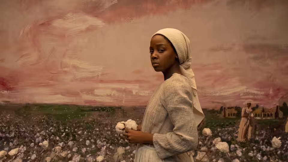 Cora (Thuso Mbedu) holding cotton bolls in a vast field under pink sky