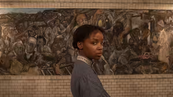 Cora (Thuso Mbedu) standing before a large mural on a tiled wall