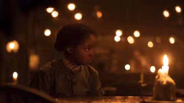 Cora (Thuso Mbedu) seated at a table lit by flickering candles