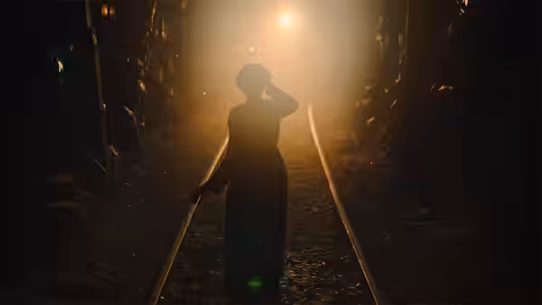 A woman walking along railroad tracks in a foggy illuminated tunnel