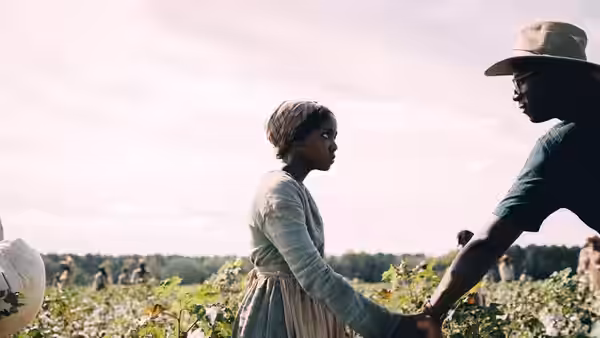 Cora (Thuso Mbedu) reaching toward a man in a sunlit field