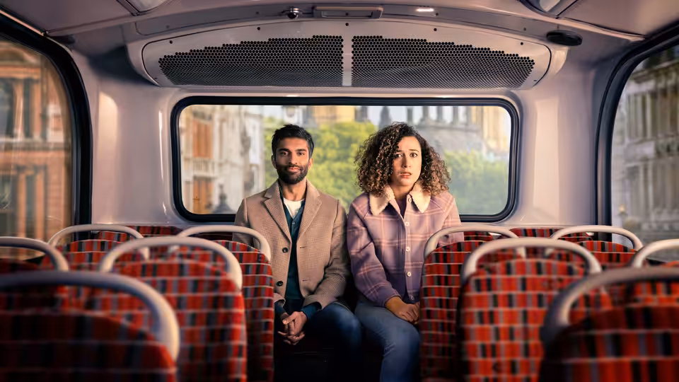 Jessie (Rose Matafeo) and Tom (Nikesh Patel) seated together on a bus