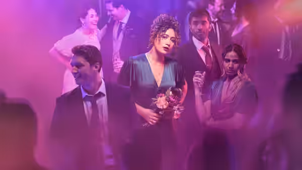 Jessie (Rose Matafeo) holding flowers beside Tom (Nikesh Patel) at a party