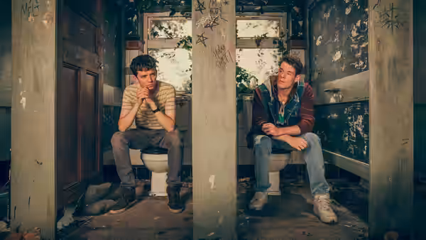 Otis (Asa Butterfield) and Adam sitting on toilets in an abandoned bathroom