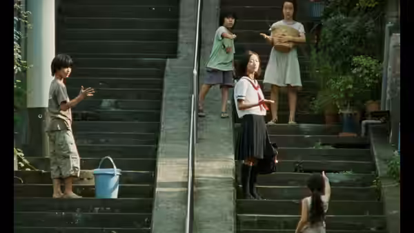 Children exchange gestures across outdoor stairways, with a bucket on the steps