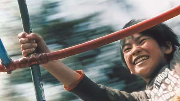 A smiling boy grips playground bars as the background blurs around him