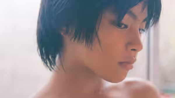 A boy gazes downward in close-up beside a softly lit window