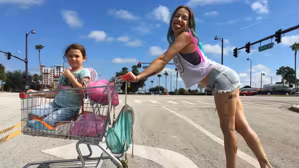Halley (Bria Vinaite) pushes Moonee (Brooklynn Prince) in a shopping cart across a parking lot