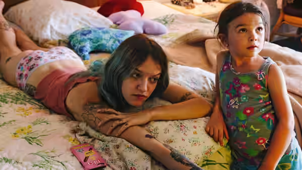 Halley (Bria Vinaite) lies on the bed beside Moonee (Brooklynn Prince) in their room