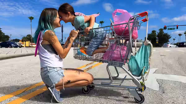 Halley (Bria Vinaite) kneels to kiss Moonee (Brooklynn Prince) in a shopping cart