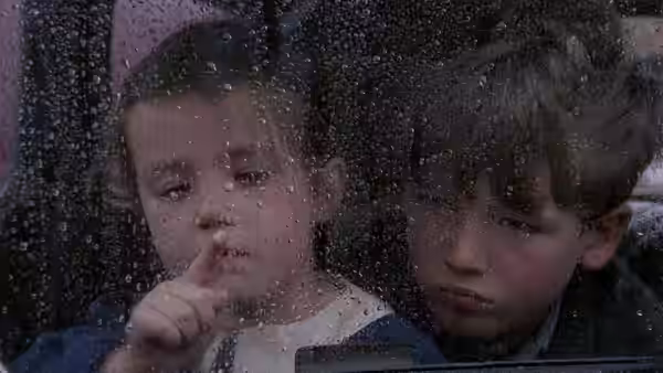 Two young boys looking out through a rain-covered window pane