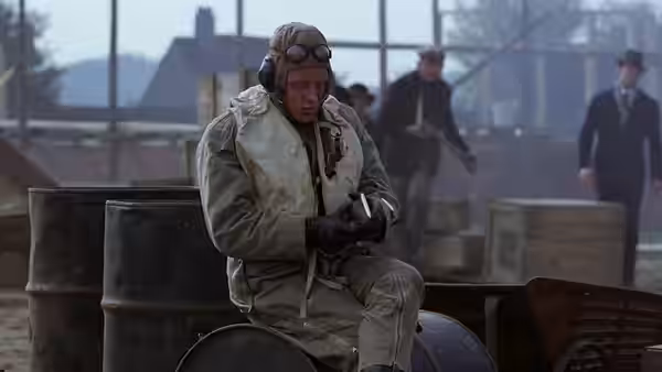 An aviator in flight gear seated on barrels at an airfield
