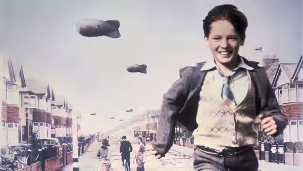 Bill (Sebastian Rice-Edwards) running along a suburban street beneath barrage balloons