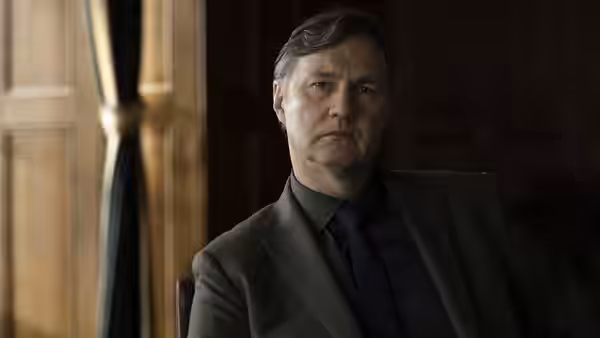 David Morrissey seated indoors in a suit with a serious expression