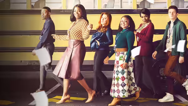 Teachers walking in front of a yellow school bus while holding papers