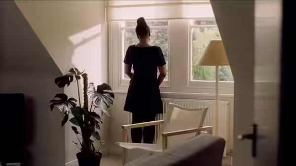 A woman standing with her back turned looking out a window
