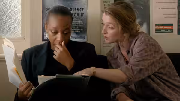 Hortense (Marianne Jean-Baptiste) and the social worker examining documents on a sofa