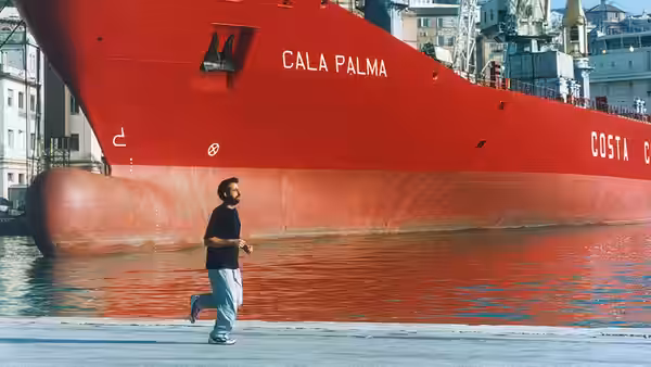 Giovanni jogs along the waterfront beside a large red cargo ship