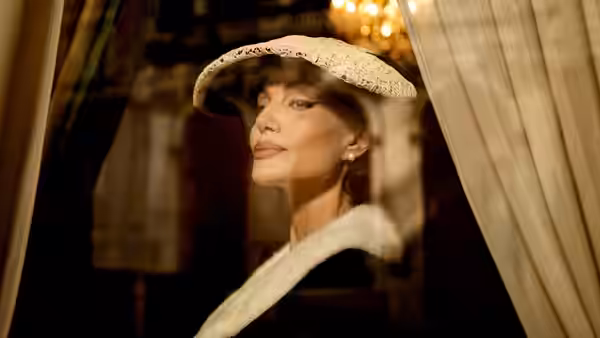 Maria Callas (Angelina Jolie) looks through a window wearing a white hat and fur