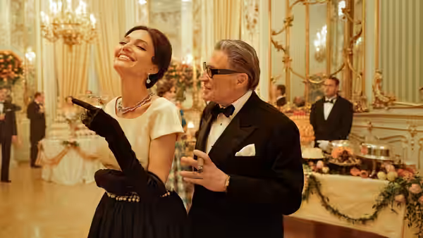 Maria Callas (Angelina Jolie) smiles beside Aristotle Onassis (Haluk Bilginer) at a gala