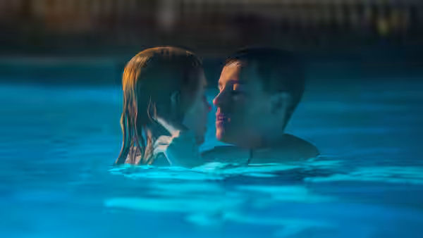 a young man and woman facing each other in a swimming pool at night