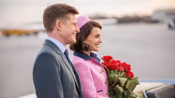 John F. Kennedy (Caspar Phillipson) and Jackie Kennedy (Natalie Portman) pose by the waterfront with roses