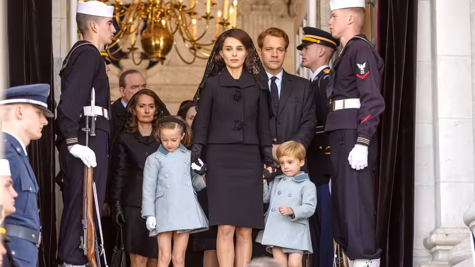 Jackie Kennedy (Natalie Portman) stands with her children and attendants at a building entrance