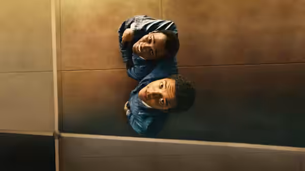 Two young men in blue jackets lying on a tiled floor looking up