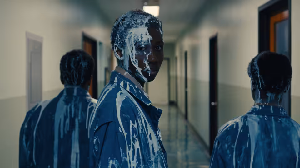 Three young men in paint-splattered blue jackets standing in a hallway