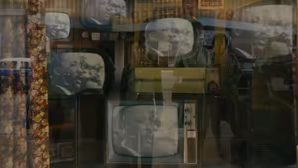 A woman and a man reflected in a store window displaying old televisions