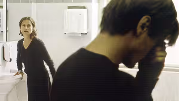 Erika Kohut (Isabelle Huppert) looking at a man in a bathroom