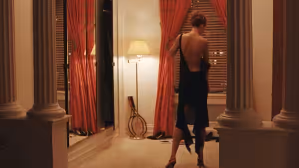 A woman in a black dress standing before red curtains and mirrors